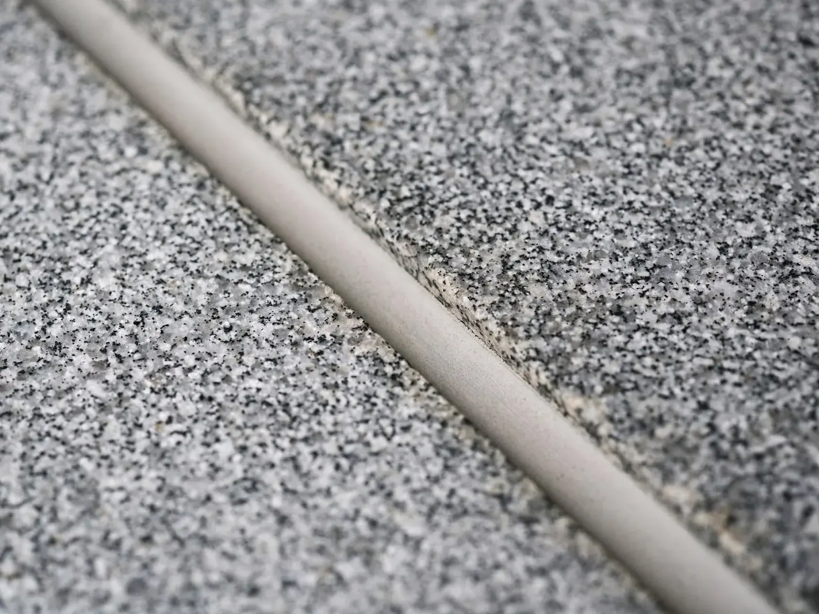 Macro d’un joint de mortier clair traversant en diagonale deux blocs de granit gris moucheté